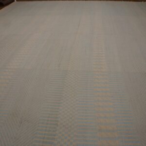 Large flatweave rug with a repeating tan and pale blue striped geometric pattern on a wood floor.