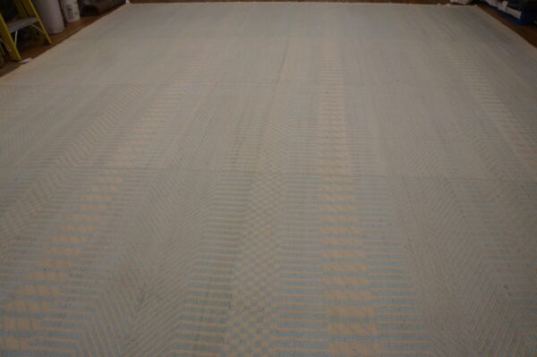 Large flatweave rug with a repeating tan and pale blue striped geometric pattern on a wood floor.