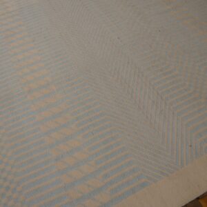 Beige and pale blue flatweave rug featuring an intricate geometric star pattern rests on dark wooden flooring.