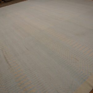 Large low-pile rug featuring an angular geometric pattern in light beige and powder blue on wood flooring.