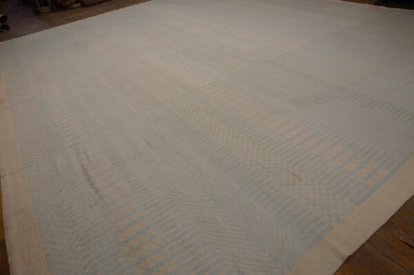 Large low-pile rug featuring an angular geometric pattern in light beige and powder blue on wood flooring.