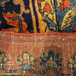 Close-up showing the navy, red, and gold pile of a rug folded over its tight woven backing.