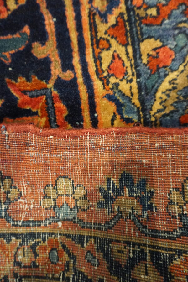 Close-up showing the navy, red, and gold pile of a rug folded over its tight woven backing.