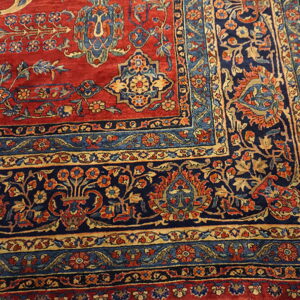 Corner detail of a red and navy rug showing intricate floral patterns and multiple colored borders.