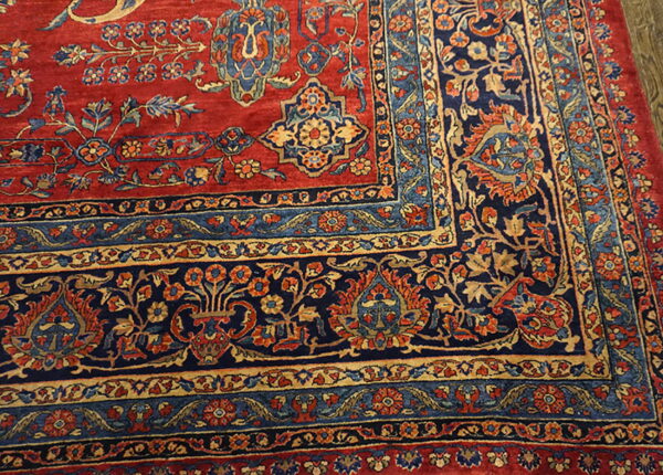 Corner detail of a red and navy rug showing intricate floral patterns and multiple colored borders.