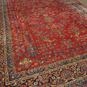 High-pile red rug with intricate navy, gold, and blue traditional design on grey wood flooring.