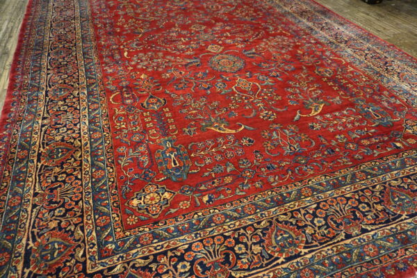 High-pile red rug with intricate navy, gold, and blue traditional design on grey wood flooring.