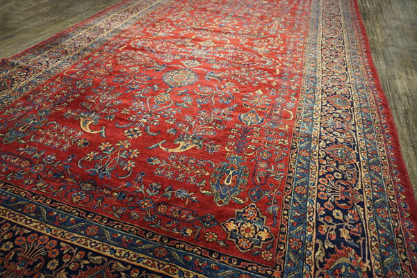 Red rug featuring intricate blue and gold floral designs and multiple borders on gray wood floors.