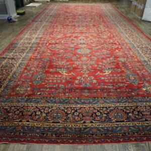 Oversized red runner rug with dense traditional blue and gold motifs displayed on dark wood planks.