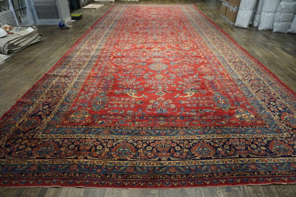 Oversized red runner rug with dense traditional blue and gold motifs displayed on dark wood planks.