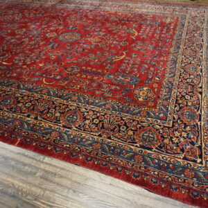 Red, navy, and gold patterned rug with a detailed floral border over distressed wood flooring.