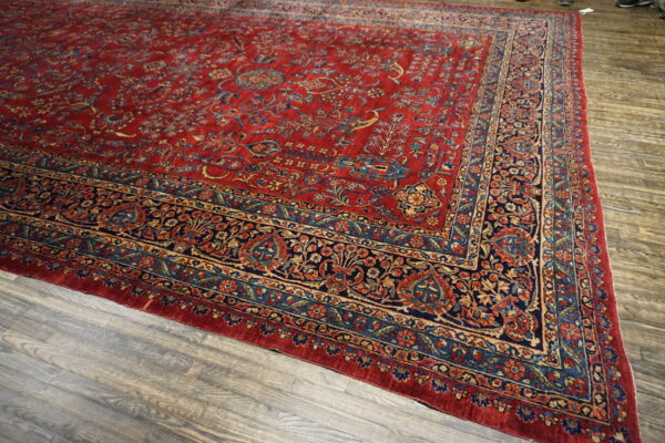 Red, navy, and gold patterned rug with a detailed floral border over distressed wood flooring.