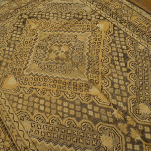 Geometric patterned rug in tan and deep brown rests on distressed wood plank flooring.