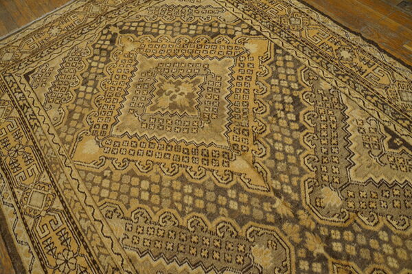 Geometric patterned rug in tan and deep brown rests on distressed wood plank flooring.