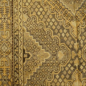 Distressed rug detail showing complex geometric patterns and borders in faded gold and dark earth tones.