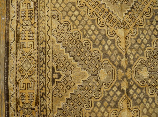 Distressed rug detail showing complex geometric patterns and borders in faded gold and dark earth tones.