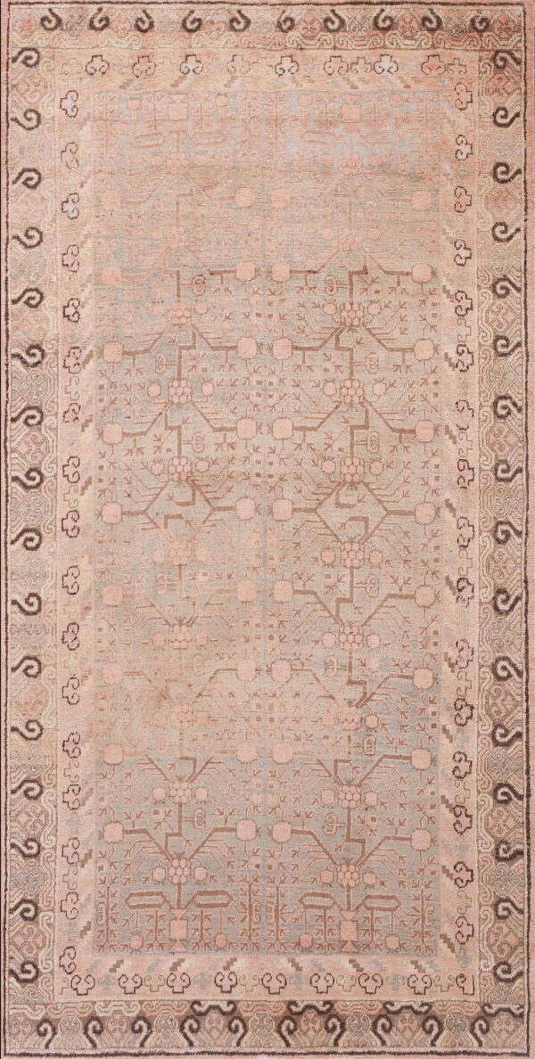 A faded pink and pale blue rug with a dense geometric pattern and multiple ornate borders.