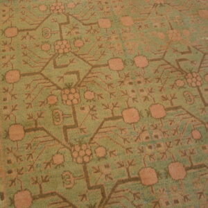 Detailed view of a low-pile rug featuring faded olive green and dusty peach geometric patterns.
