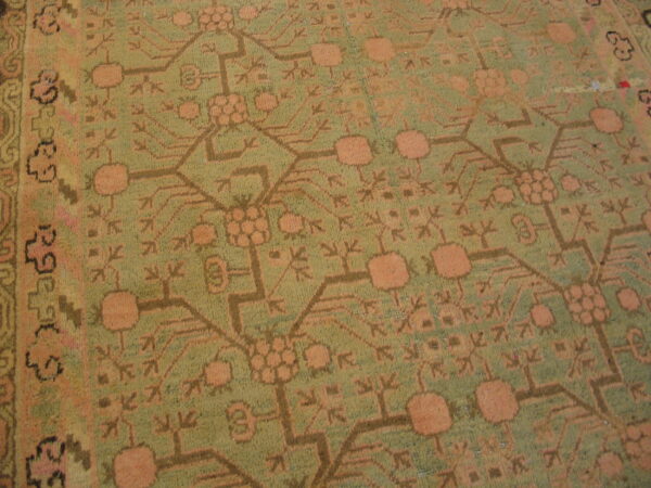 Detailed view of a low-pile rug featuring faded olive green and dusty peach geometric patterns.