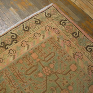 Traditional pink and green patterned rug with fringe and stylized border on distressed wood planks.