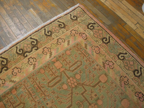 Traditional pink and green patterned rug with fringe and stylized border on distressed wood planks.