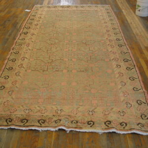Distressed geometric rug in muted green and pink with dark borders displayed on wood flooring.