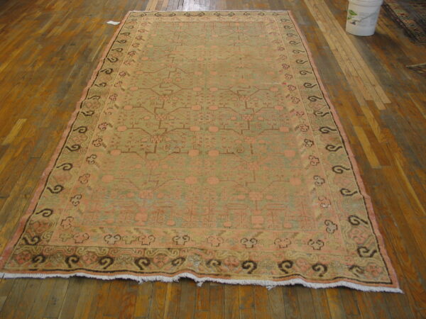Distressed geometric rug in muted green and pink with dark borders displayed on wood flooring.