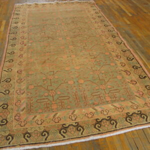 Traditional low-pile rug in sage green and peach geometric patterns lies on a warm plank hardwood floor.