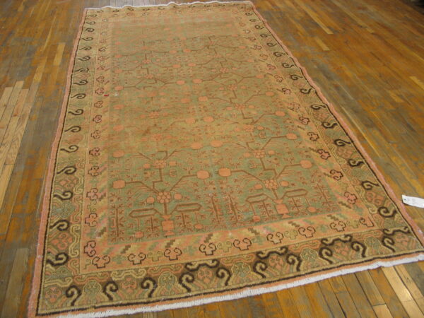 Traditional low-pile rug in sage green and peach geometric patterns lies on a warm plank hardwood floor.