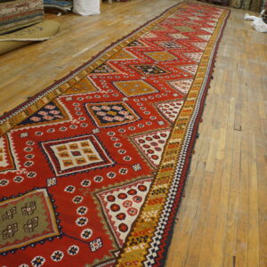 Flatweave runner with large red, yellow, olive, and navy geometric medallions displayed on aged wood flooring.