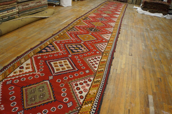 Flatweave runner with large red, yellow, olive, and navy geometric medallions displayed on aged wood flooring.