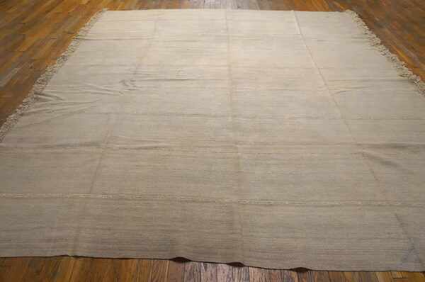 Neutral tan flatweave rug featuring subtle horizontal stitched lines on dark hardwood floors.