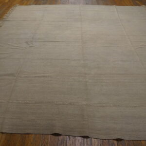 Light beige flatweave rug with visible horizontal seams and side fringe covers a polished hardwood floor.