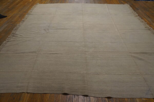 Light beige flatweave rug with visible horizontal seams and side fringe covers a polished hardwood floor.