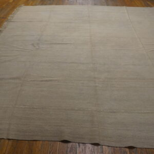 A large light beige flatweave rug with fringes and horizontal stitched seams lies on a hardwood floor.