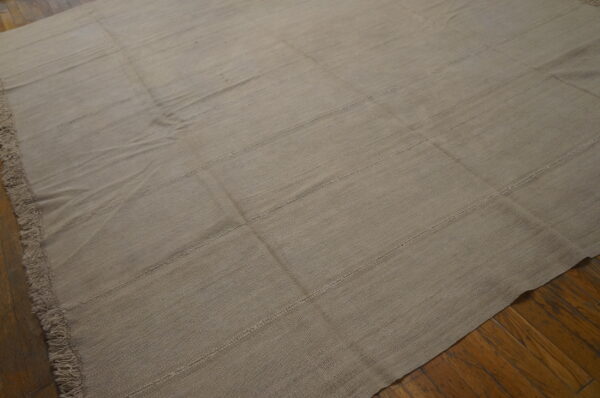 Taupe flatweave rug with horizontal seams and fringe displayed on distressed wood planks.