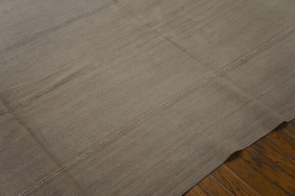 A textured taupe flatweave rug with horizontal seams rests on dark hardwood floors.