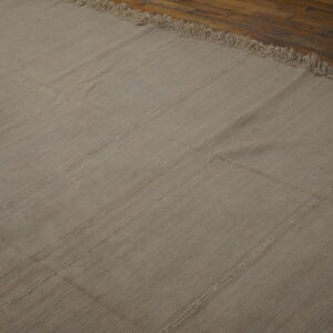 A neutral flatweave rug featuring visible vertical seams and fringe rests on dark wood planks.