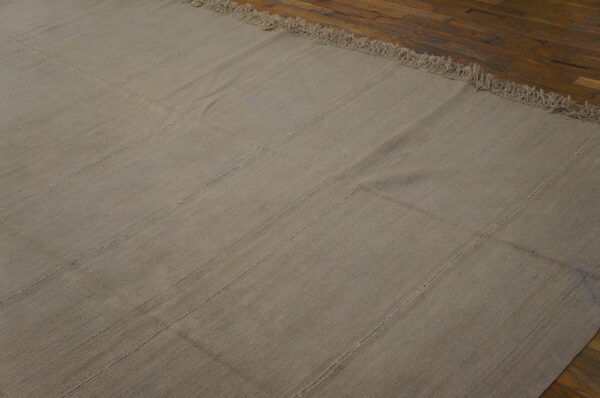 A neutral flatweave rug featuring visible vertical seams and fringe rests on dark wood planks.