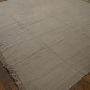 Monochromatic light beige flatweave rug with stitched seams and fringe rests on a dark brown hardwood floor.