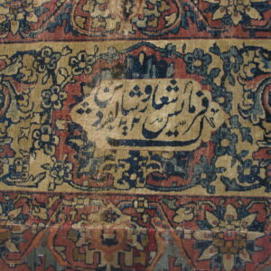 Detailed view of a multi-bordered rug in tan, red, and navy with a central calligraphic panel.