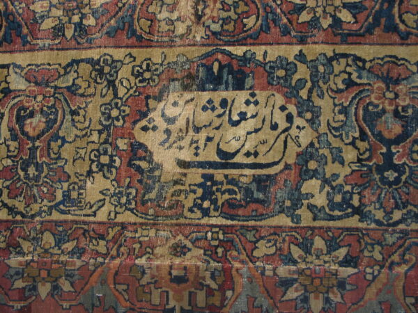 Detailed view of a multi-bordered rug in tan, red, and navy with a central calligraphic panel.