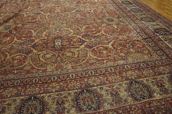 Ornate rug with complex floral patterns in deep red, tan, and dark blue on wood flooring.