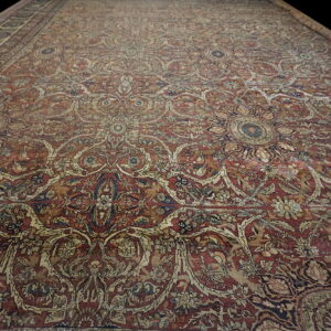 Ornate red and tan rug with a low pile featuring intricate floral medallions on a dark background.