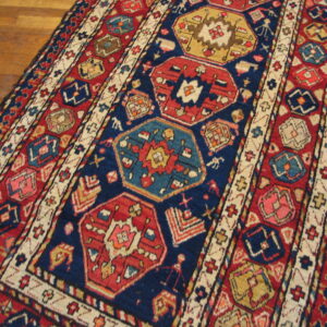 Navy blue and red geometric rug featuring octagonal medallions rests on polished wood floorboards.