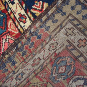 High-pile red, blue, and cream geometric rug section joins a lower-pile border in muted gray and tan.