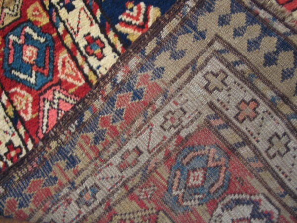 High-pile red, blue, and cream geometric rug section joins a lower-pile border in muted gray and tan.