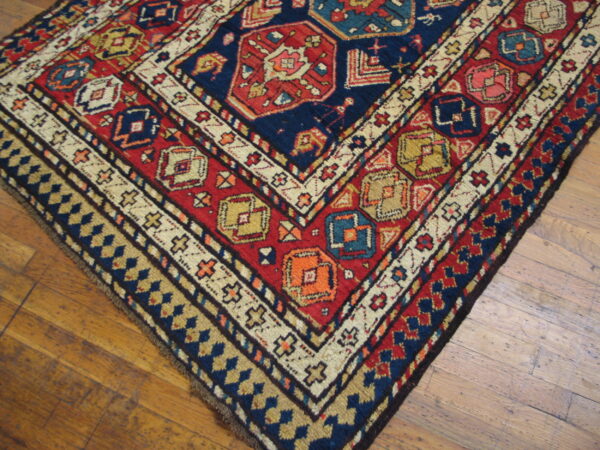 Geometric rug in navy, crimson, cream, and gold with a multi-bordered pattern covers a wooden floor.
