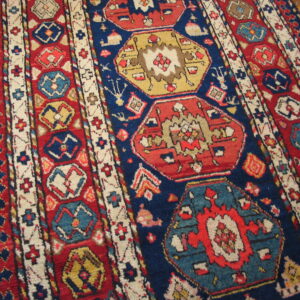 Red and blue rug featuring geometric medallions and border details on a wood floor.
