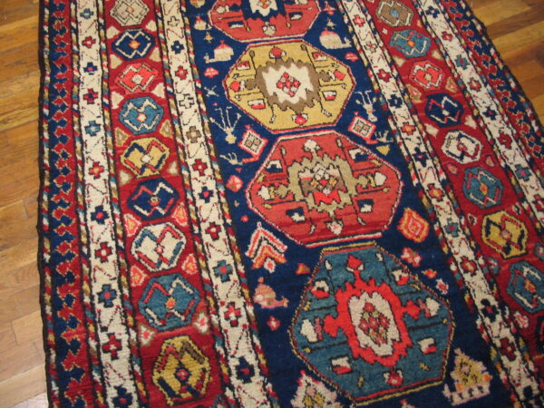 Red and blue rug featuring geometric medallions and border details on a wood floor.